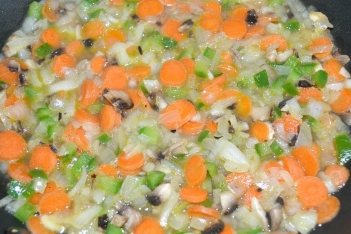 Chopped carrots, onions, bell peppers, and mushrooms sautéing in a pan.