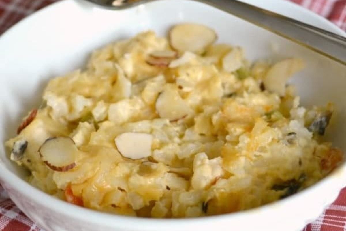 A white bowl filled with a creamy garden chicken casserole topped with sliced almonds, placed on a red plaid cloth.