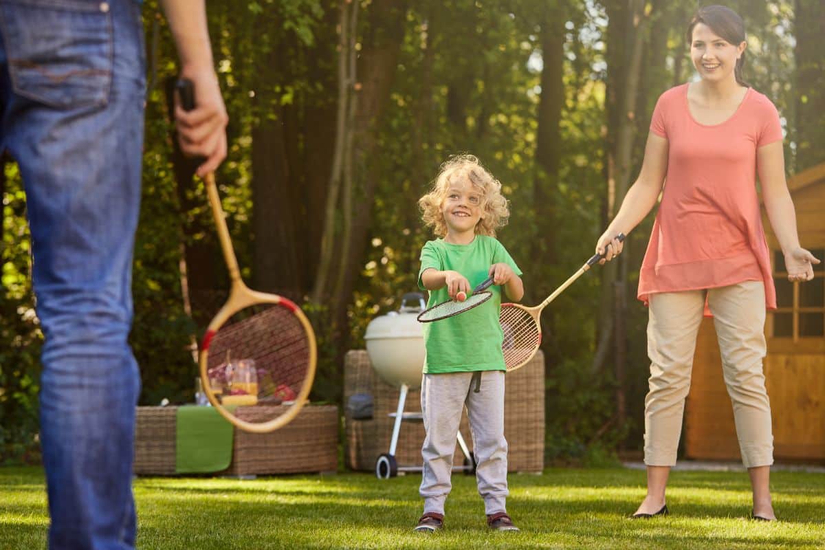 A family engaging in games you can play with your kids instead of exercising, enjoying a game of badminton in the backyard.