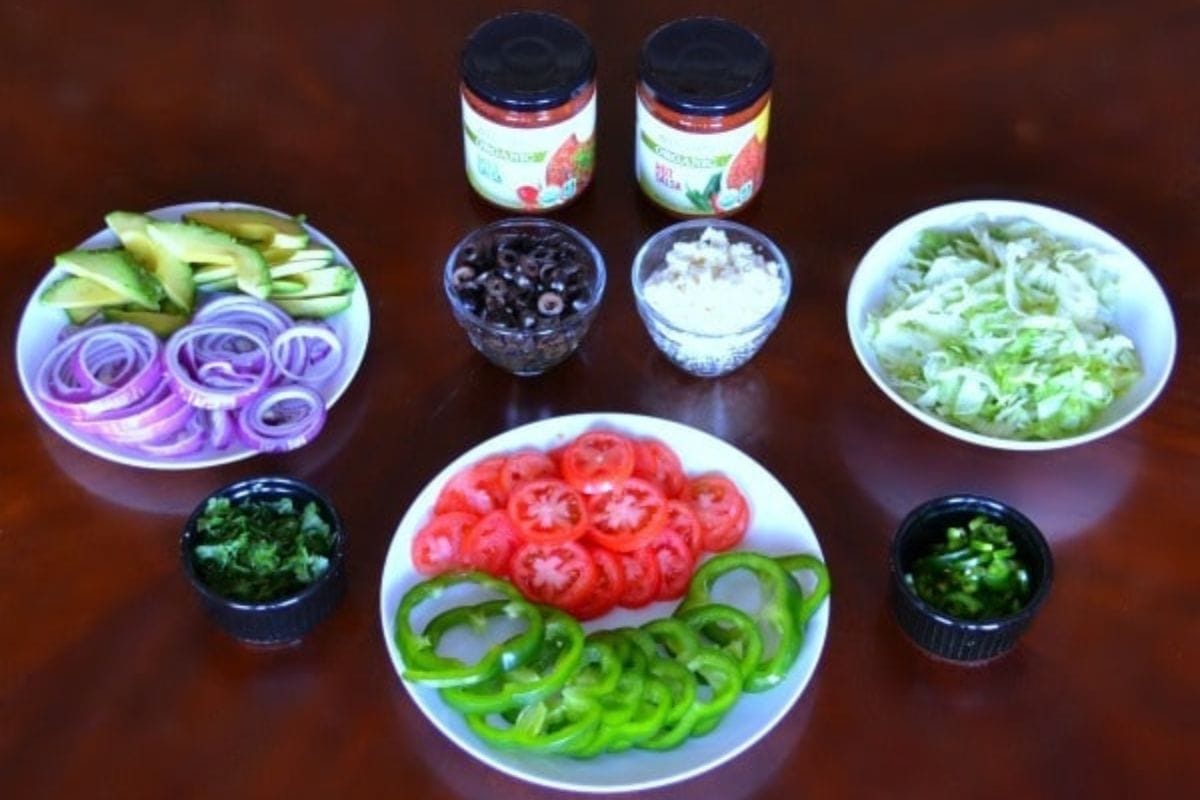 Chicken Tostada Toppings in bowls and on plates on a brown table.