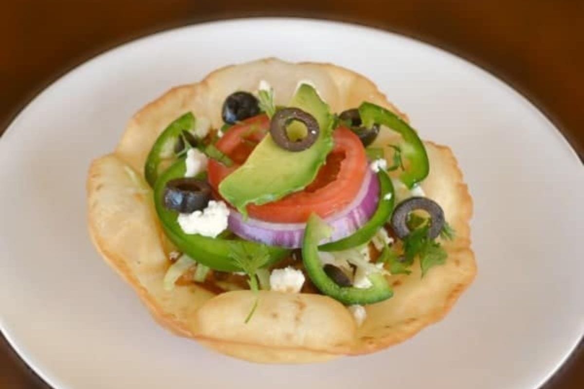 Chicken Tostada on a white plate on a brown table.