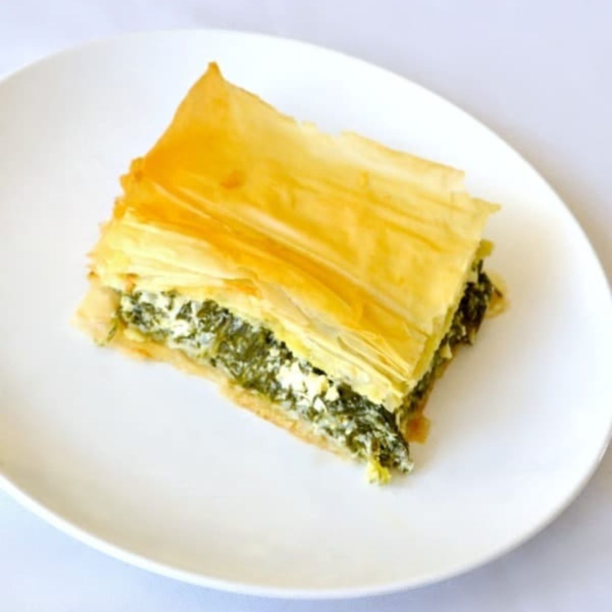 A slice of spinach and cheese pie with flaky phyllo pastry layers served on a white plate.