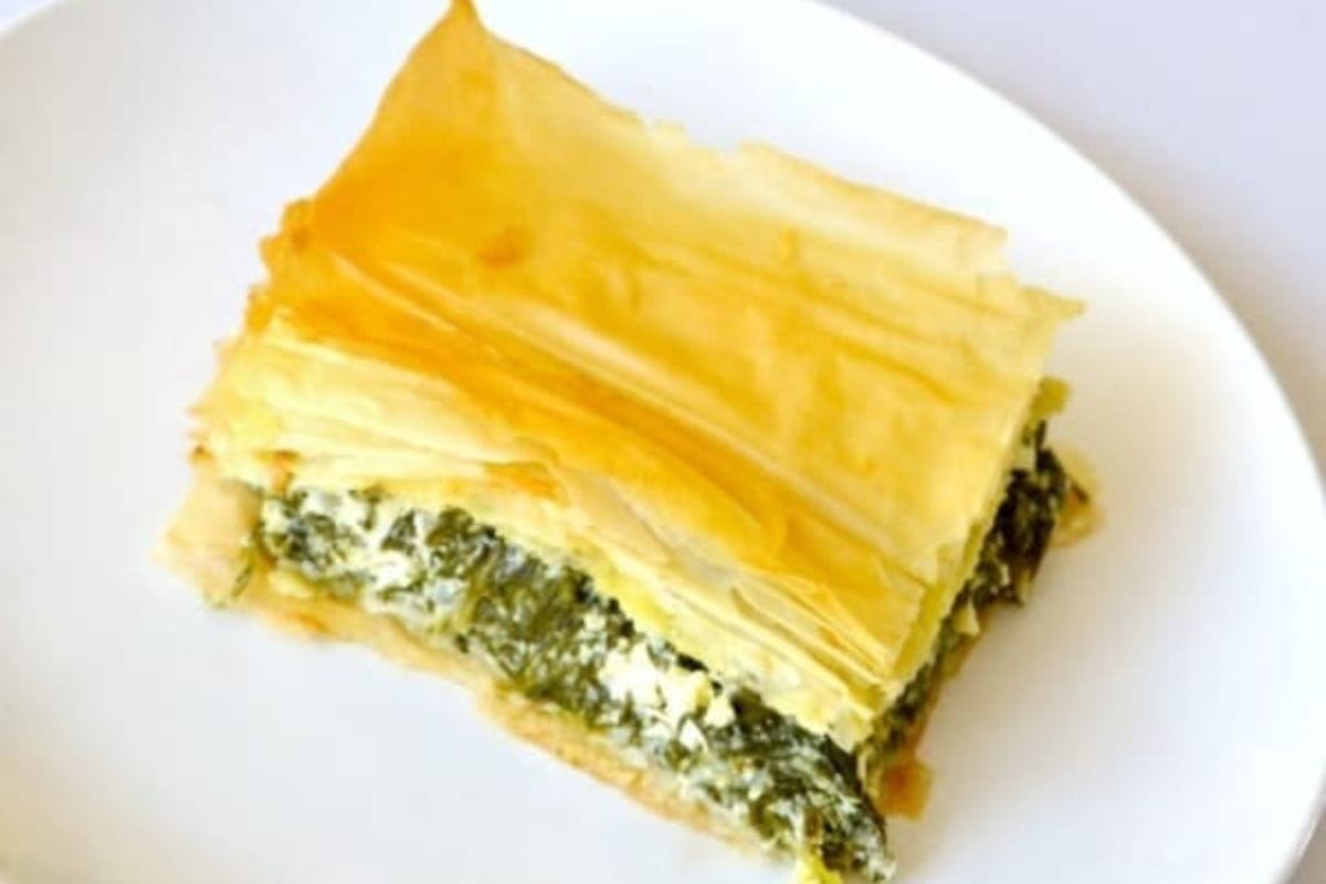 A slice of spinach feta pie with flaky golden phyllo pastry layers on a white plate.