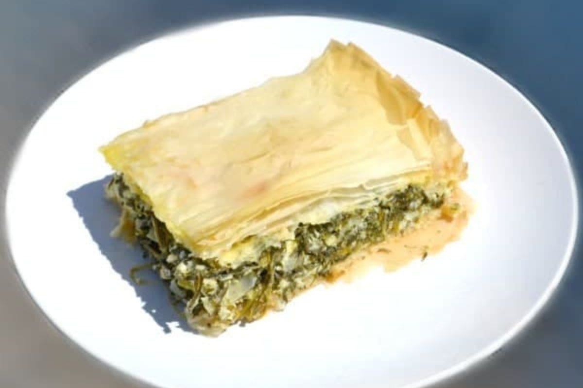 A slice of spinach and feta pie with layers of flaky pastry on a white plate.