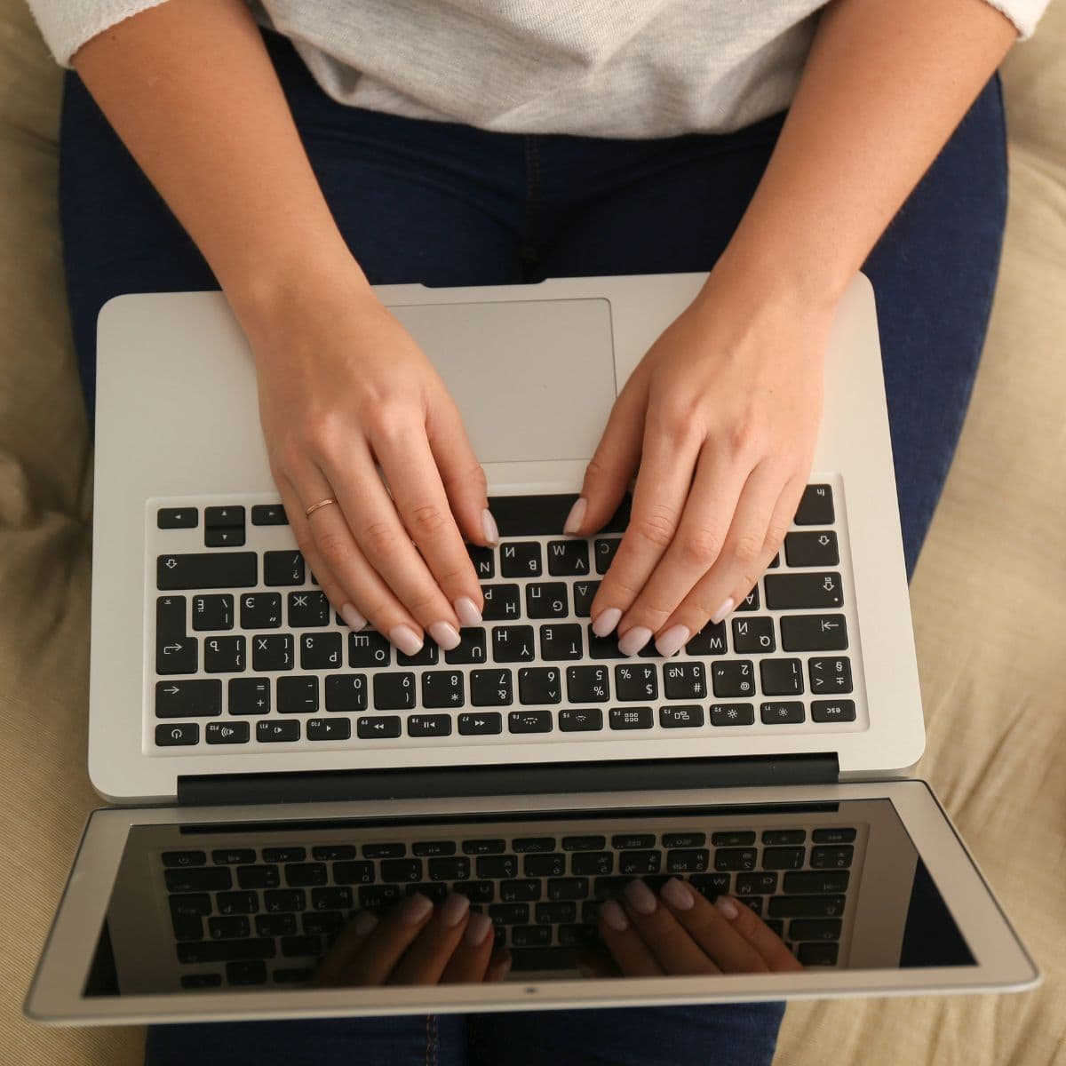 A person types on a laptop keyboard while sitting on a beige couch, viewed from above, focused on a blog post stockpile challenge.