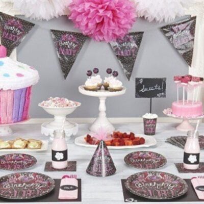 A birthday party table with pink and black decorations, party hats, cupcakes, a large cupcake cake, sweets, and charming "Birthday Girl" plates and banners creates a sweet chalkboard party theme.