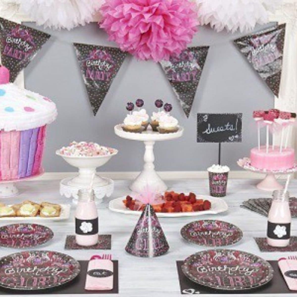 A birthday party table with pink and black decorations, party hats, cupcakes, a large cupcake cake, sweets, and charming "Birthday Girl" plates and banners creates a sweet chalkboard party theme.
