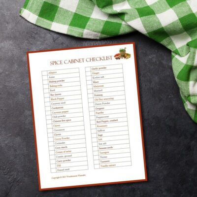 A spice cabinet checklist is printed and rests on a dark countertop beside a green and white checkered cloth.