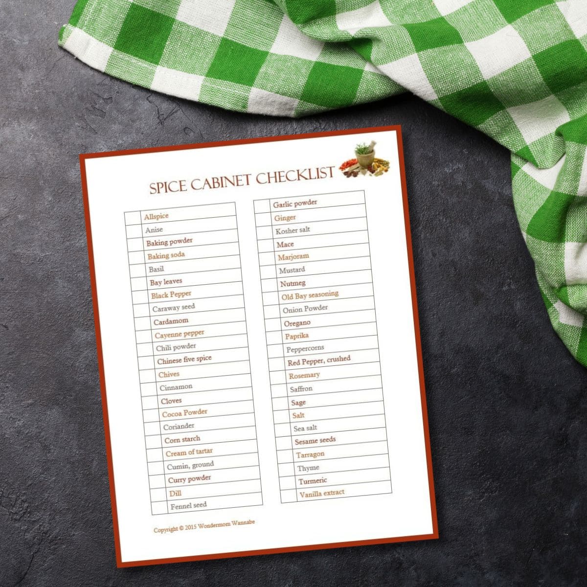 A spice cabinet checklist is printed and rests on a dark countertop beside a green and white checkered cloth.