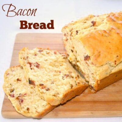 A loaf of bacon bread rests on a wooden cutting board, with two slices cut and placed in front. The text "Bacon Bread" appears in the upper left corner, showcasing this savory homemade treat.