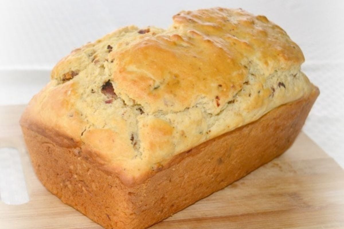 A loaf of homemade bacon bread, resting on a wooden cutting board.