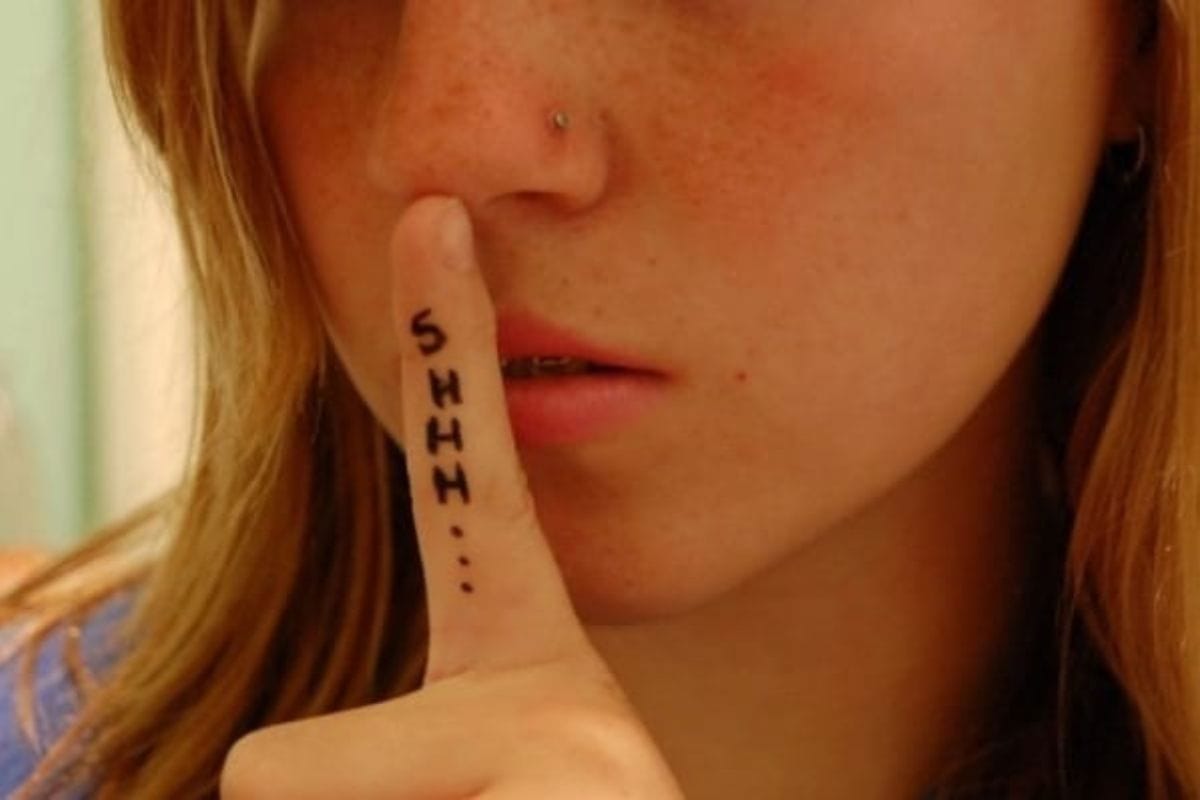 A person holds a finger to their lips in a shushing gesture, with