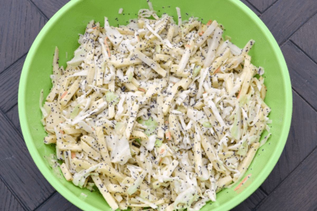Green bowl filled with apple coleslaw salad-shredded cabbage and apples tossed with poppy seeds and creamy dressing-resting on a dark wooden surface.