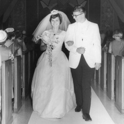 A bride in a white gown and veil walks arm-in-arm with a groom in a white jacket down the aisle of a church, both smiling, ready to begin their journey together and embrace the 10 habits of a healthy marriage, with guests seated along the sides.
