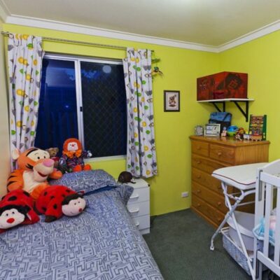 A brightly colored children's bedroom with a single bed, plush toys, crib, dresser, and patterned curtains on a window—perfect for safe & cozy kids rooms.