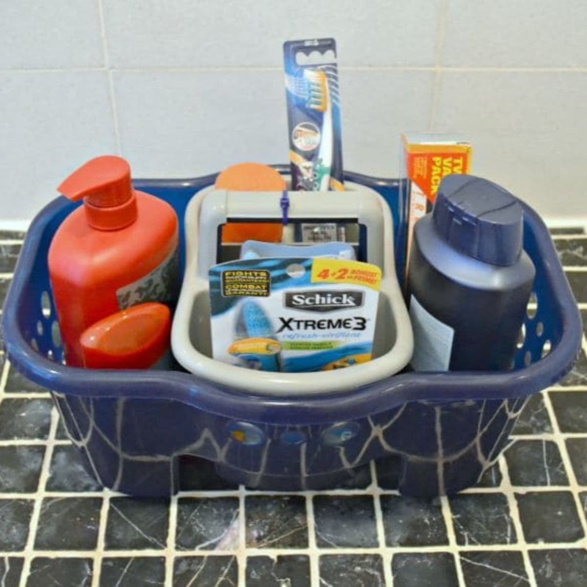 A blue caddy filled with shaving and hygiene products, including a red pump bottle, razors, a toothbrush, and a dark blue bottle—perfect for a college care package.
