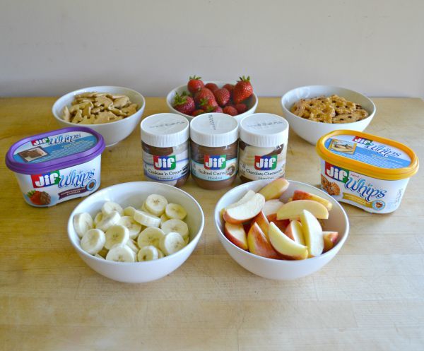 fruit and crackers in white bowls and jif whips and spreads on a brown table as end of summer Snackation Snacks