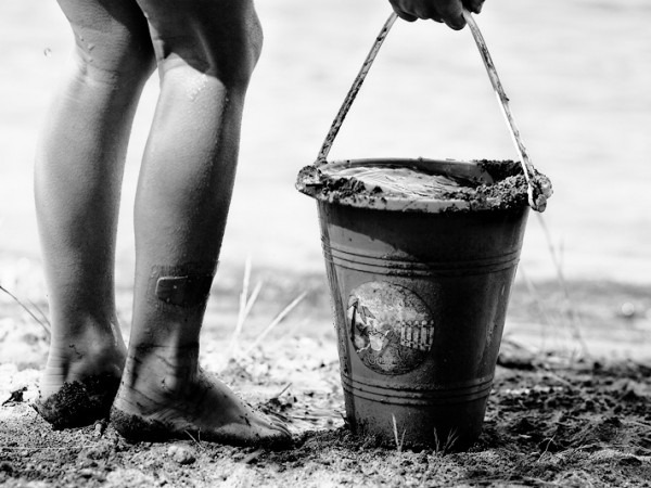 a child holding a sand bucket at a beach as Tips for Getting Through the Summer with Kids