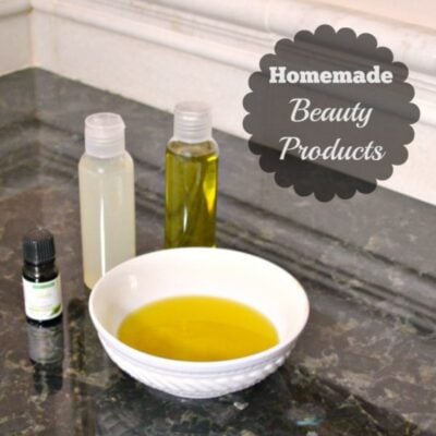 A white bowl with yellow liquid and three small bottles, one labeled, sits on a dark countertop with text reading “Homemade Beauty Products” featuring rosemary essential oil.
