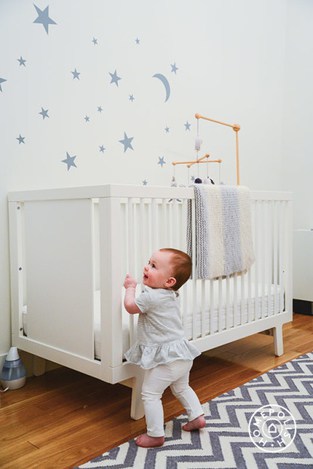 Star stickers on wall behind white crib with baby standing against it