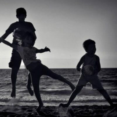 Three children play and jump on a beach at sunset, their silhouettes outlined against the sea and sky—a perfect example of how to get kids to be more physically active in a fun, natural setting.