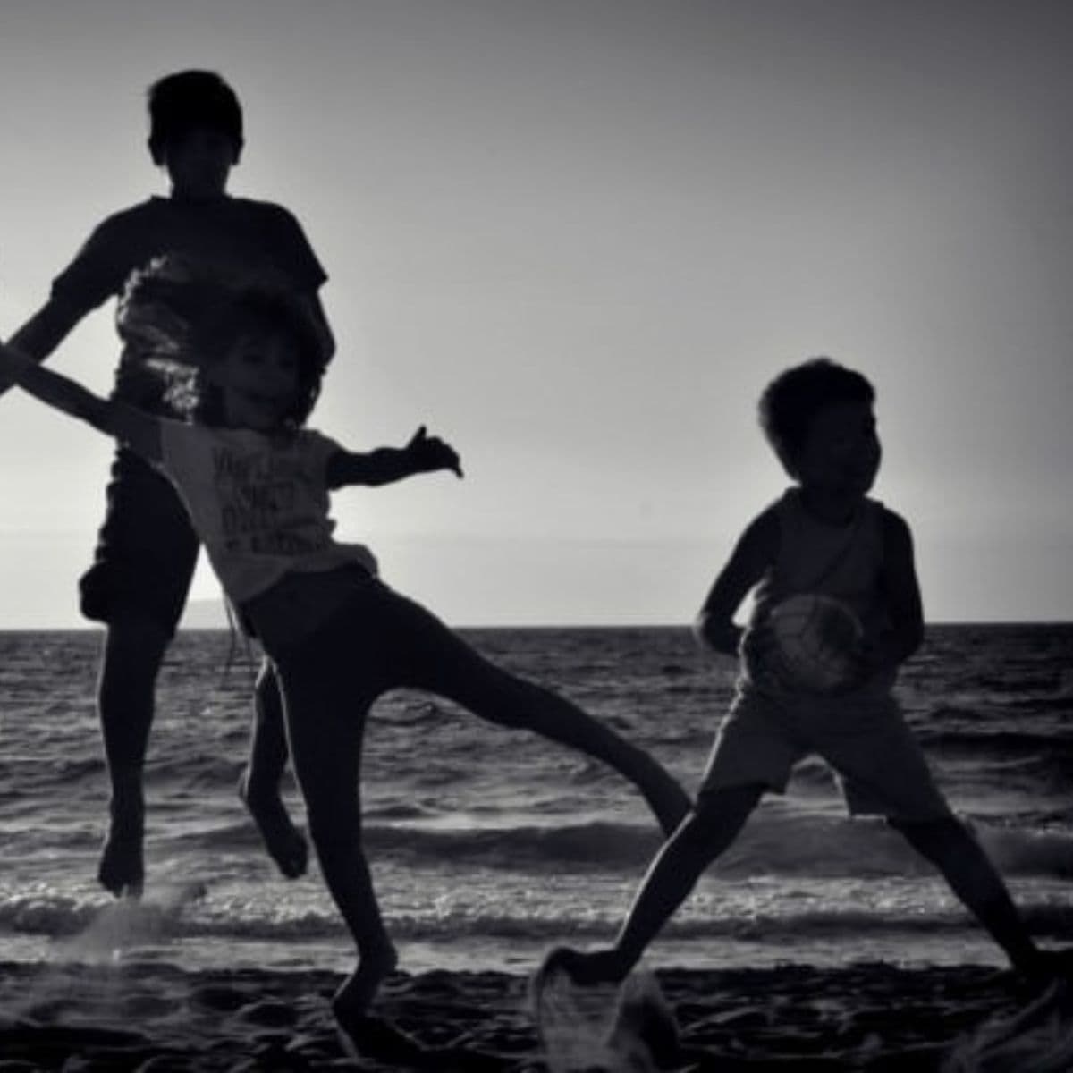 Three children play and jump on a beach at sunset, their silhouettes outlined against the sea and sky—a perfect example of how to get kids to be more physically active in a fun, natural setting.