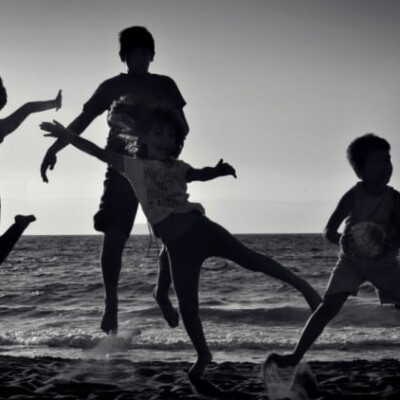 Black and white photo of 4 kids jumping in the sand