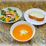 Bowl of soup, bowl of salad, and plate with slice of bread