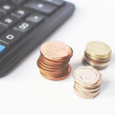 Stacks of assorted coins are placed next to a calculator on a white surface, symbolizing smart budgeting and exploring ways to save money online.