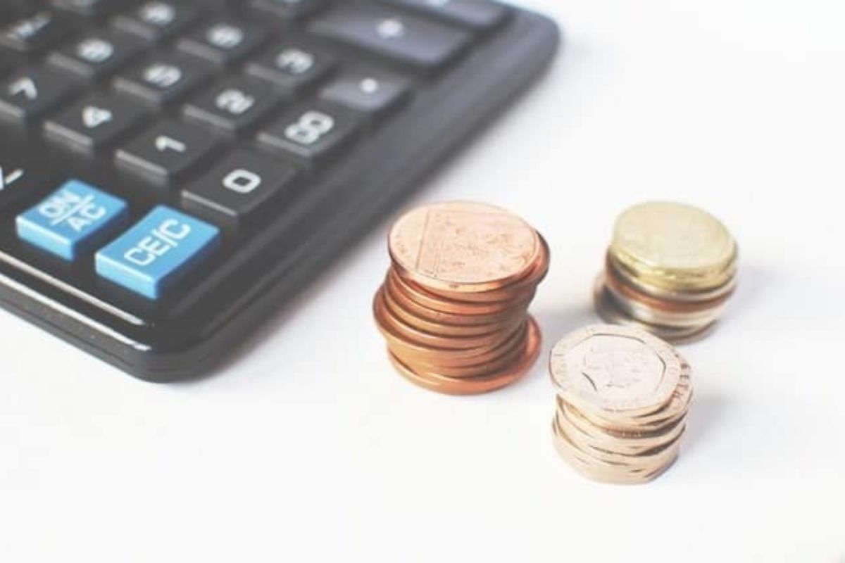 A close-up of a calculator next to small stacks of assorted coins on a white surface.