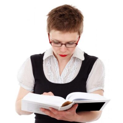Person with short hair and glasses, wearing a black vest over a white shirt, reading an open book against a white background to improve brain function.