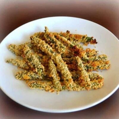 A white plate with several crispy baked green beans, arranged in a loose pile and coated in a golden breaded crust.