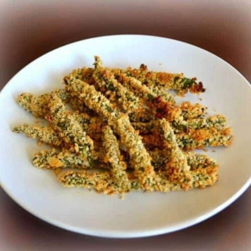A white plate with several crispy baked green beans, arranged in a loose pile and coated in a golden breaded crust.