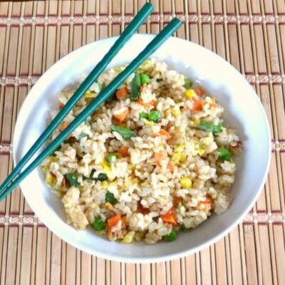 A bowl of veggie fried rice with peas, carrots, corn, and green beans, served with green chopsticks on a bamboo mat.