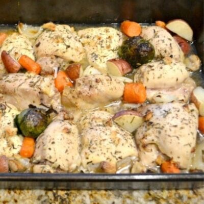 Herb roasted chicken and vegetables: Baked chicken thighs with carrots, Brussels sprouts, and red potatoes in a glass baking dish.
