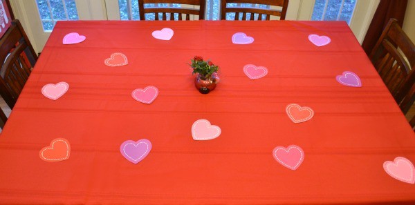 a table with a red tablecloth on it with Paper Heart Decorations on it