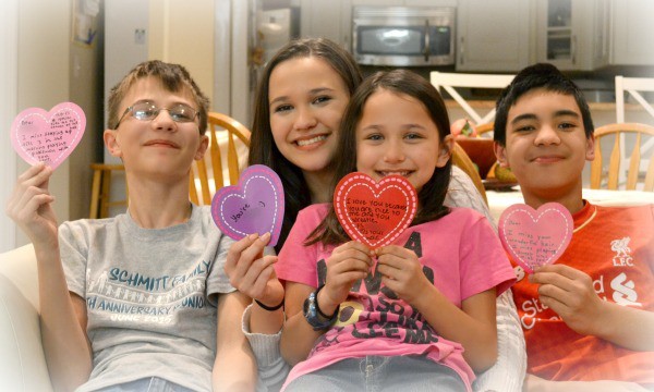 four kids holding hearts with Reasons We Love You written on them as a family Valentine's Day idea