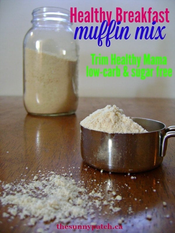 a measuring cup of muffin mix with a jar of muffin mix in the background, all on a brown table with title text reading Healthy Breakfast muffin mix