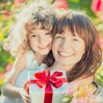 Mom and daughter smiling and holding a wrapped gift and flowers