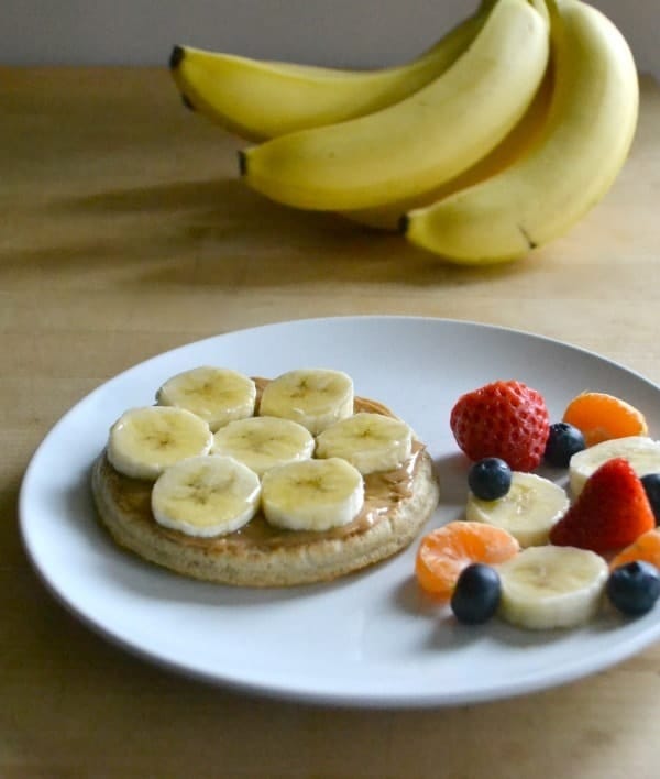 Banana breakfast Pizza on a white plate on a wood table with bananas in the background