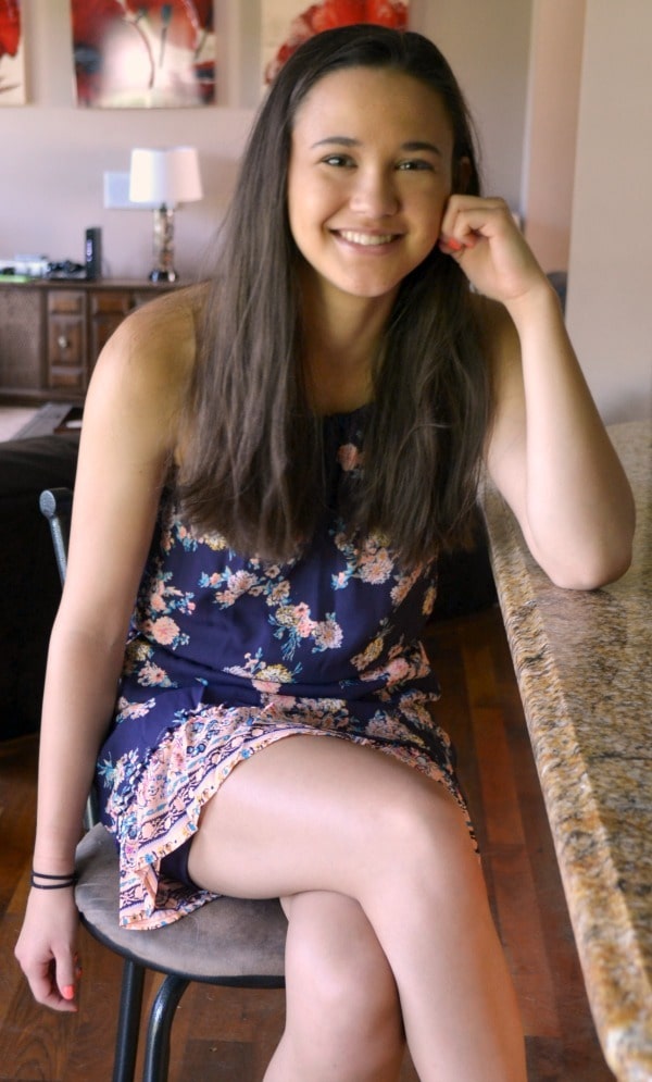a teen girl wearing a dress sitting on a barstool at a kitchen counter