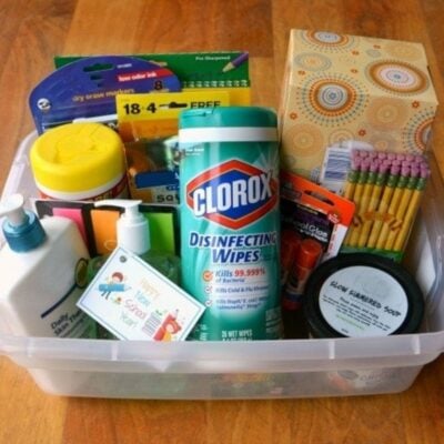 Plastic bin filled with school supplies, including disinfecting wipes, pencils, tissues, glue, sticky notes, soap, markers, and dry erase markers—a thoughtful option for back to school gift ideas for teachers.