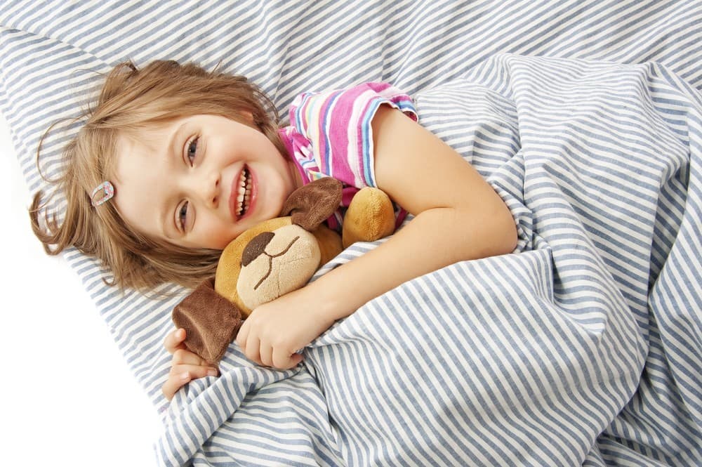 a girl and her stuffed dog laying in a bed