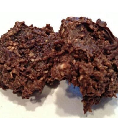 Two no-bake chocolate oatmeal cookies on a white surface, their rough, textured appearance highlighting visible oats and rich chocolate—a delicious example of a simple chocolate protein cookie recipe.