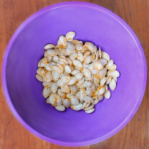 pumpkin seeds in a purple bowl on a brown table