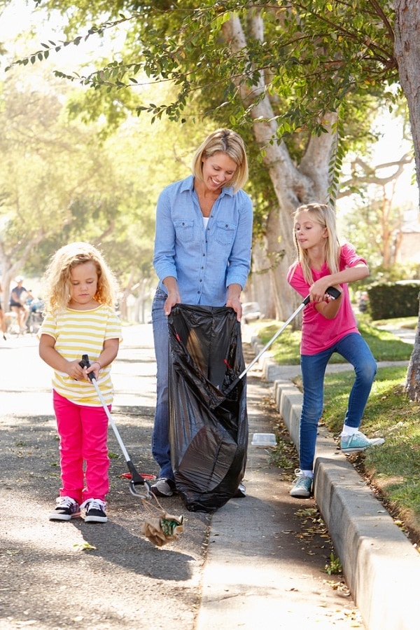 a mom and her two daughters outside picking up trash on a street