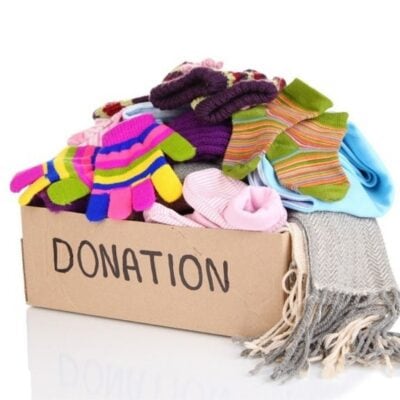 A cardboard box labeled "DONATION" filled with colorful gloves, socks, scarves, and winter clothing items—perfect for teaching children charity and the importance of helping others in need.