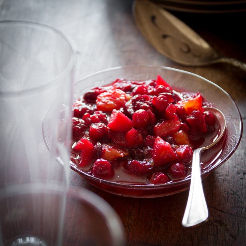 Cranberry Sauce with Apples and Oranges in a glass bowl with a spoon in it on a brown table