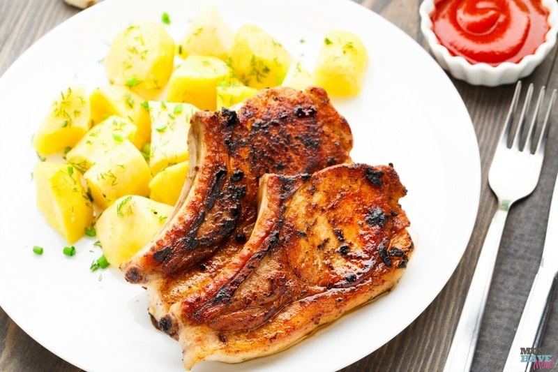 instant pot bbq pork chops next to yellow squash on a white plate on a brown table next to a fork and knife and a white bowl of ketchup