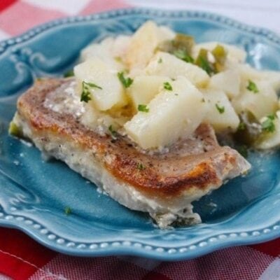 A baked pork chop topped with creamy potatoes and fresh herbs is served on a blue plate.